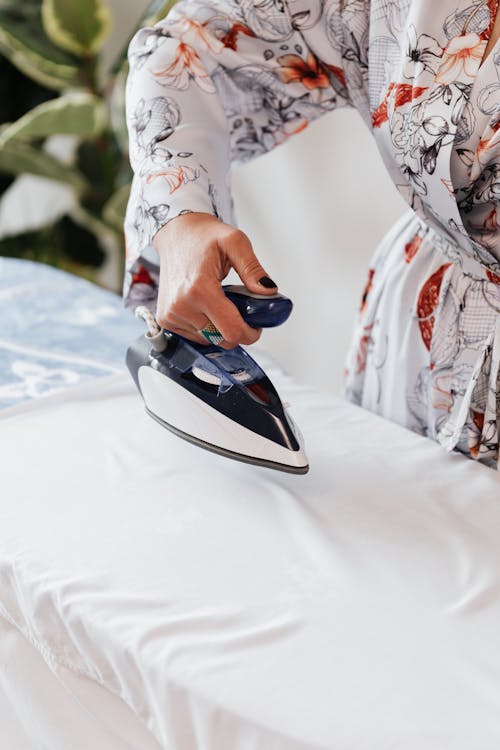 Crop housewife ironing white clothes on ironing board