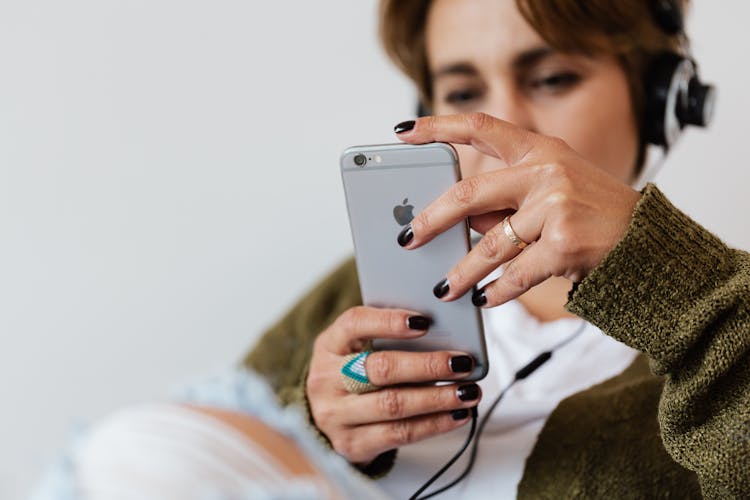 Crop Woman Using Smartphone And Listening To Music In Headphones