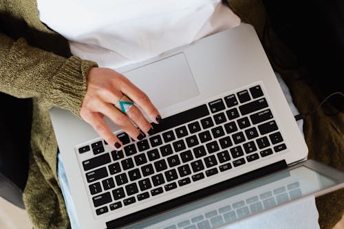 Free Top view crop anonymous female wearing knitted casual jacket and stylish ring typing on modern netbook keyboard Stock Photo