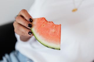 Crop unrecognizable female with manicure in white t shirt eating sweet juicy watermelon