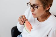 一位穿着白衬衫的女子在室内吃着西瓜，轻松惬意的夏日氛围扑面而来