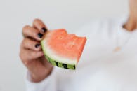 Bitten slice of fresh sweet juicy watermelon in hand of crop faceless female in white sweater