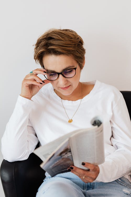 Focused adult female reading magazine in armchair