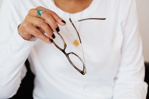 Free Crop faceless lady with manicure in white sweater holding stylish eyeglasses in hand while sitting in armchair Stock Photo
