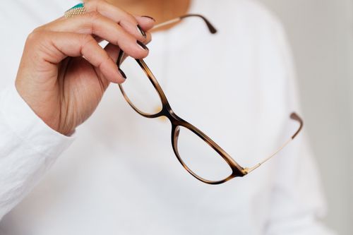 Free Crop unrecognizable elegant woman in white sweater and trendy optical glasses with brown frames and golden temples in hand Stock Photo