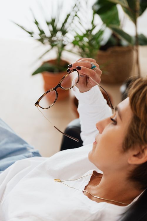 Free Side view of crop sad woman with eyeglasses in hand thinking about problems sitting in armchair in cozy room Stock Photo