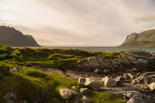 Gray Rocks on Green Grass Near Body of Water Between Mountains