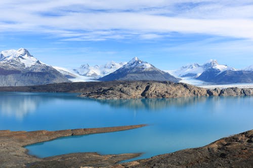 Calm lake with clean blue water reflecting snowy mountain ridge against cloudy sky in winter in highlands