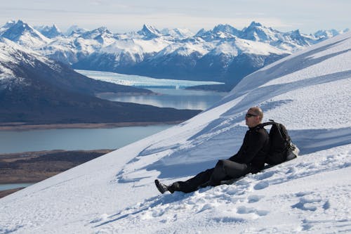 Side view of man with backpack sitting on snowy slope and resting in winter in highlands