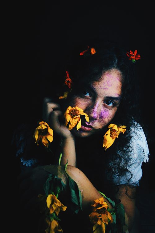 Free Young freckled woman in wreath sitting behind dried flowers and looking away in darkness Stock Photo