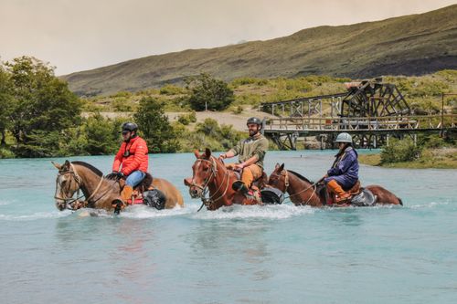 Free Group of people in helmets riding horses and crossing calm stream on gray day in hilly terrain Stock Photo