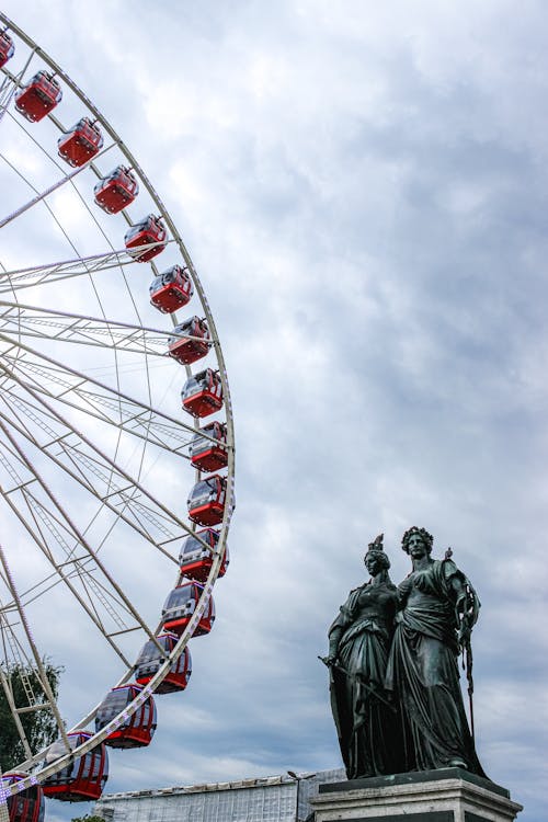 Ferris wheel near bronze monument against cloudy sky