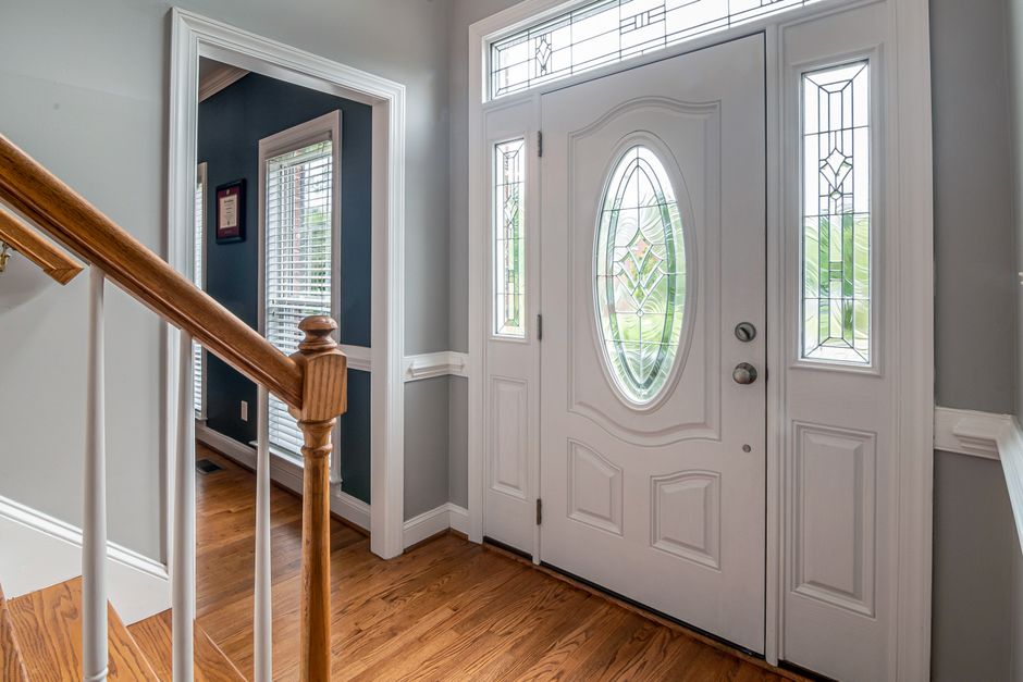 Bright and inviting home entrance featuring a white door with intricate stained glass and wooden flooring.
