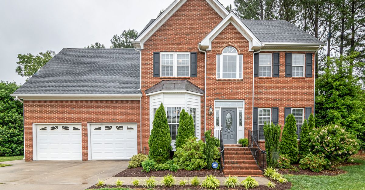 Beautiful two-story brick family house with twin garages and lush greenery.
