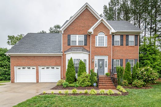 Beautiful two-story brick family house with twin garages and lush greenery.