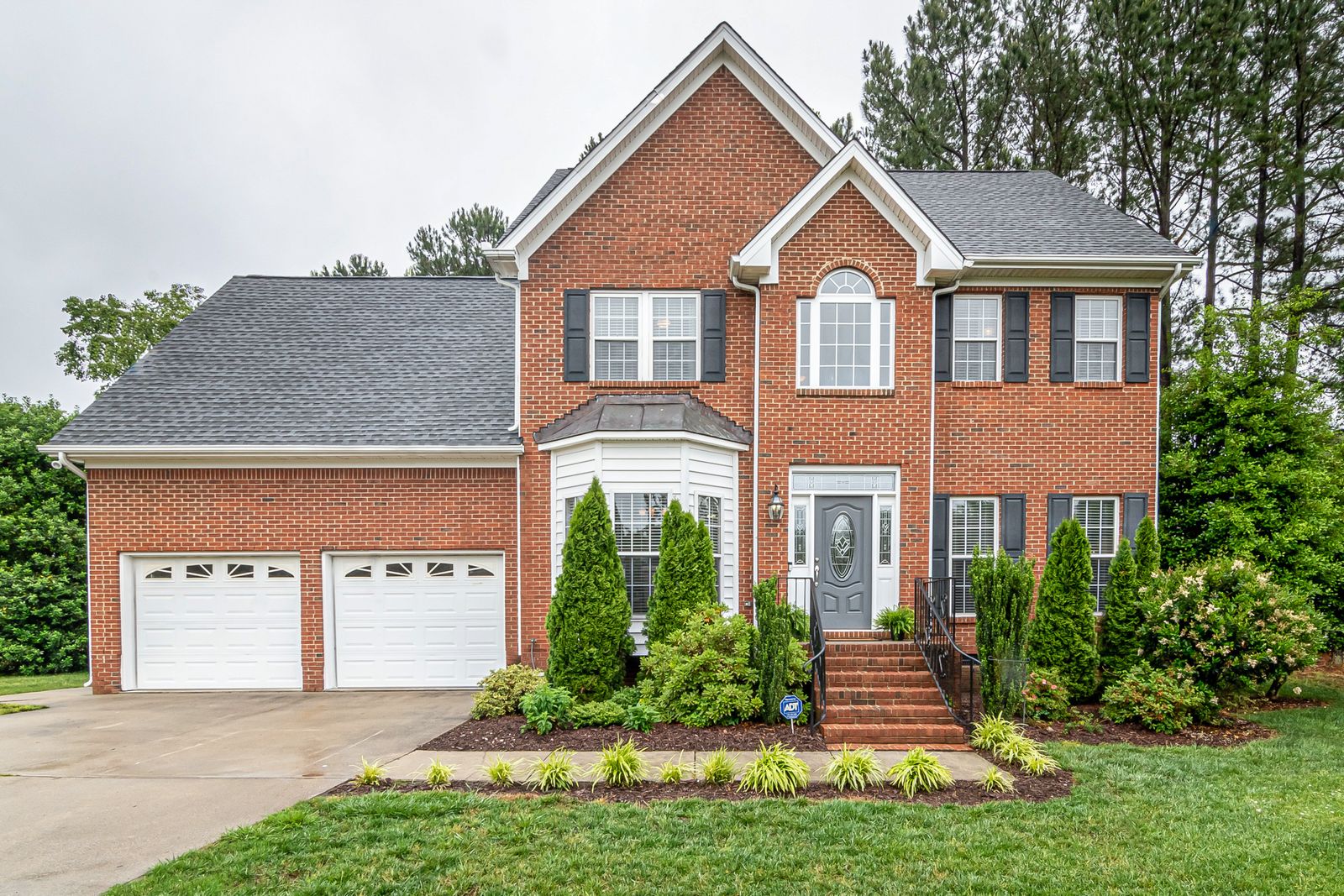 Two-story brick Colonial home with black shutters, white trim, a two-car garage, and manicured front landscaping, Ashbury, Naperville IL