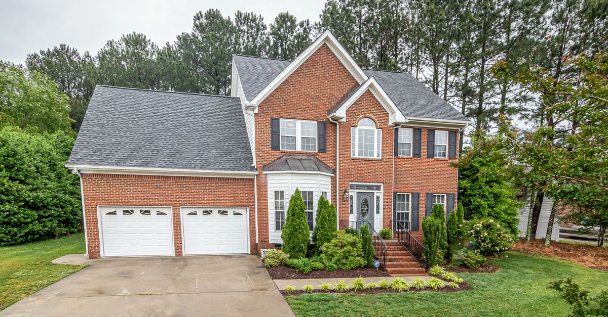 A picturesque two-story brick house in a suburban setting featuring a double garage and lush greenery.