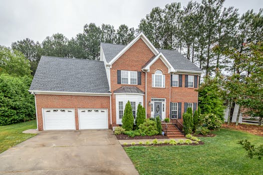 A picturesque two-story brick house in a suburban setting featuring a double garage and lush greenery.