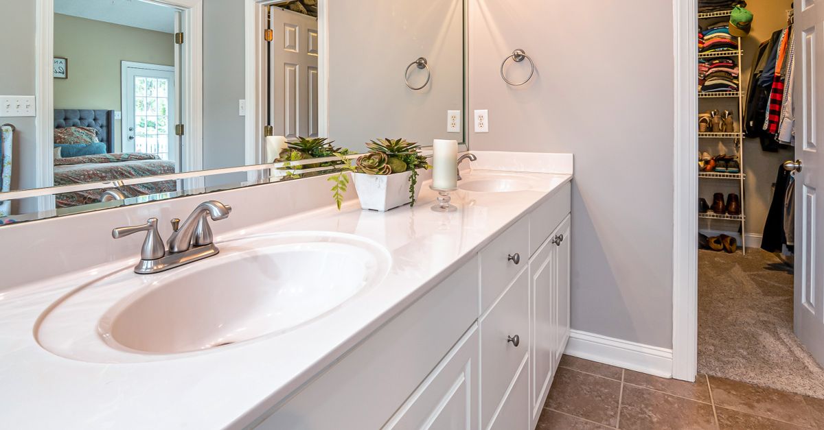 Elegant bathroom featuring white cabinets, a large mirror, and a view of the adjacent bedroom.