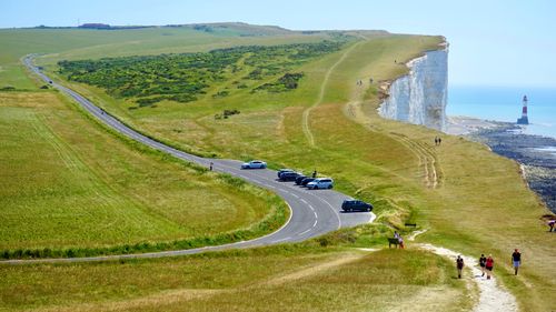Free A picturesque coastal road with a lighthouse on cliffs under a clear summer sky. Stock Photo