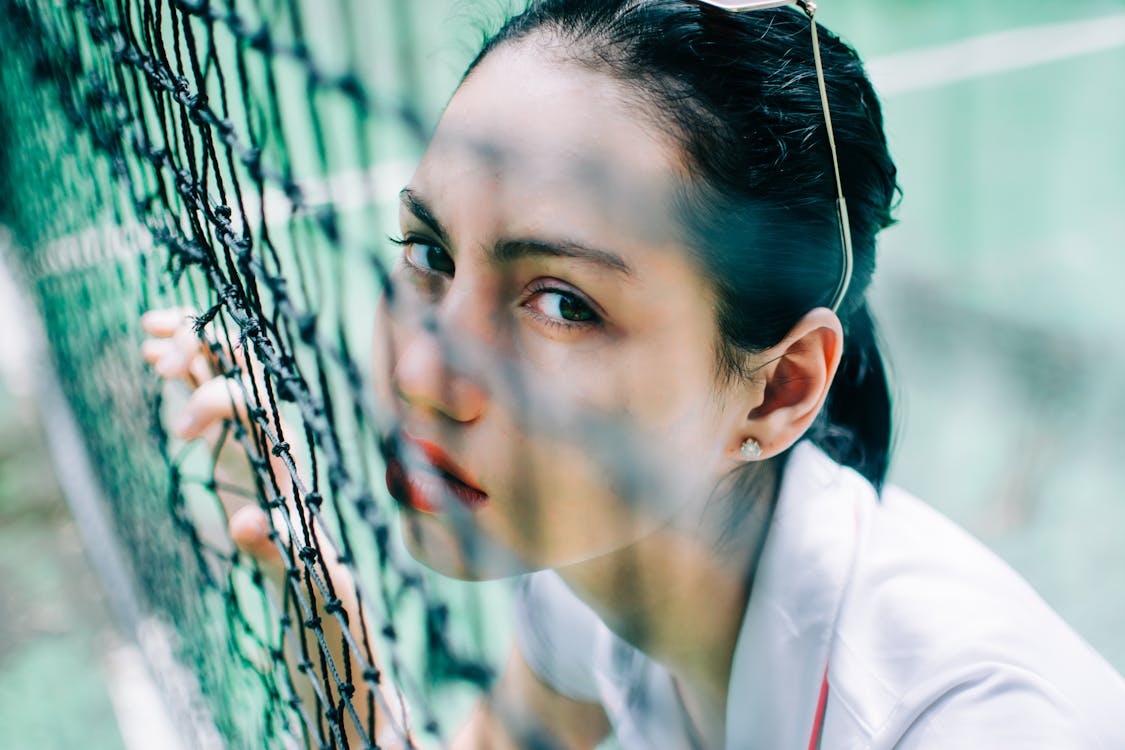 Free High angle of crop flirting female in t shirt looking at camera through net on tennis court Stock Photo