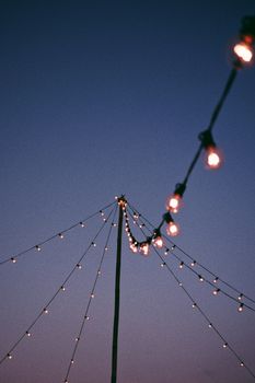 Low angle of brightly illuminated lamps of garland glowing on festive fairground against dark night sky