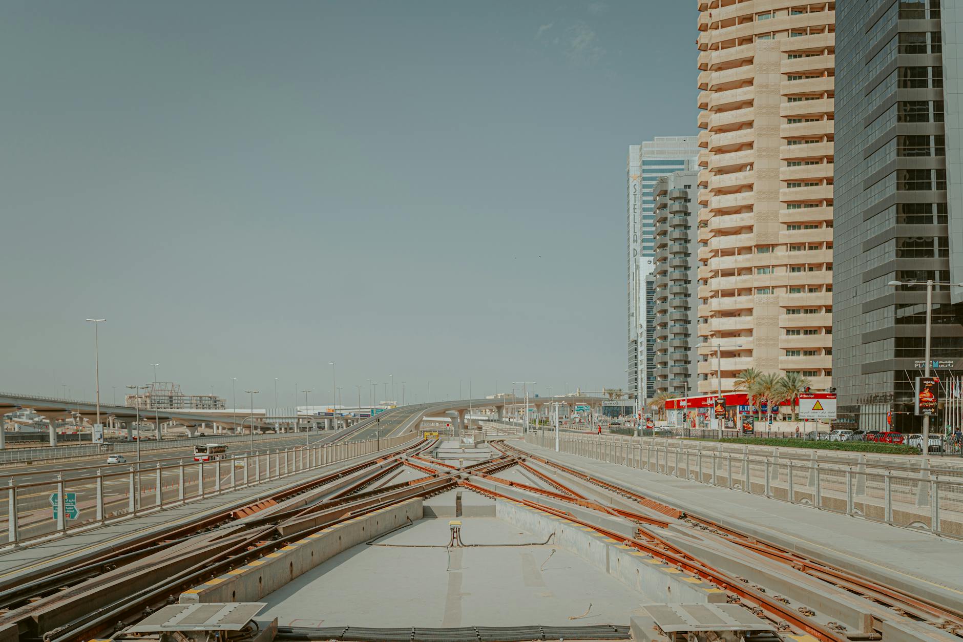 Metro tracks running through modern city along flat asphalt road and tall buildings
