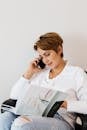 Cheerful woman talking on smartphone while reading beauty magazine