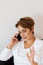 Adult female in casual wear and gold ring talking on cellphone while demonstrating objection gesture with palm of hand and looking down