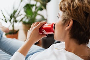 Crop unrecognizable thoughtful female enjoying coke while resting at home
