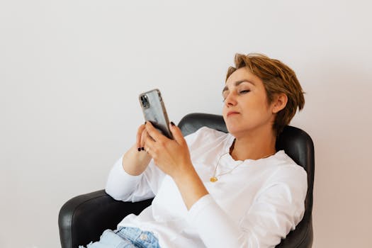 Woman in a black armchair using a smartphone, enjoying a peaceful moment indoors.