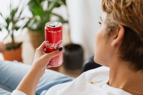 Free Side view of crop unrecognizable wistful female in casual wear lying with bright can of coke near potted plants in daylight and looking away Stock Photo