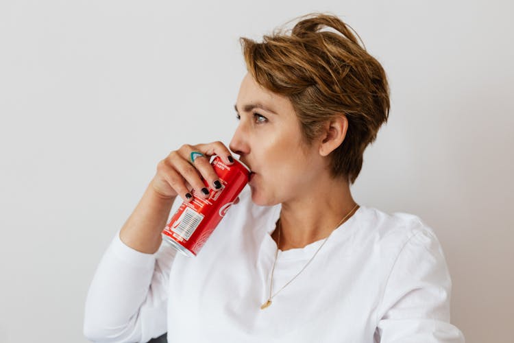 Thoughtful Woman Drinking Coke Near White Wall