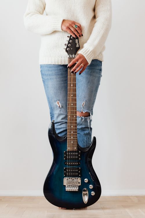 Free Crop unrecognizable female in casual jeans and white sweater standing behind modern electric guitar against white wall Stock Photo