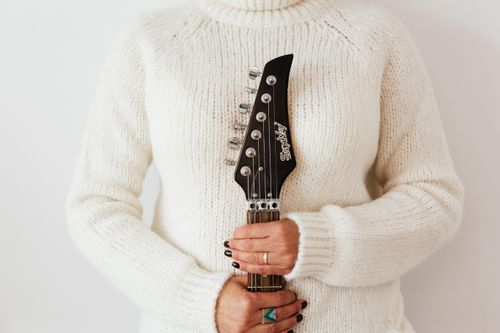 Free Crop faceless female in white knitted sweater standing against white wall with modern guitar fretboard in hands Stock Photo