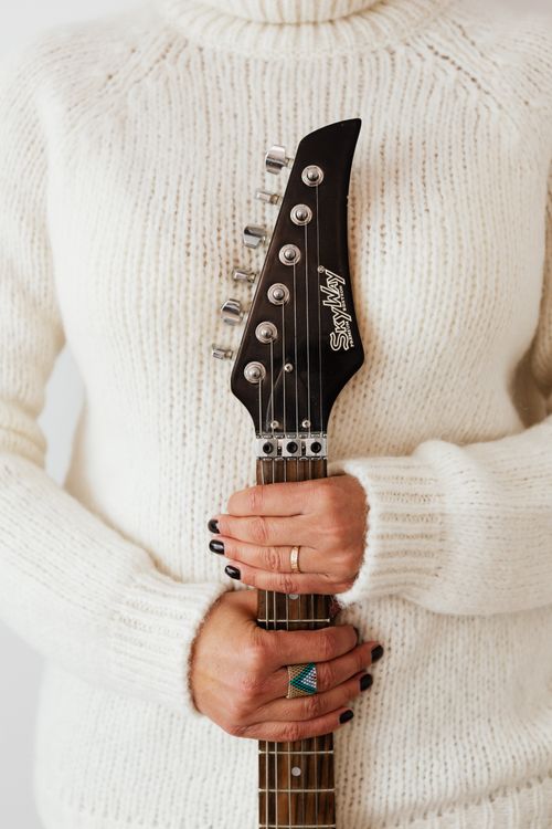 Free Crop unrecognizable female wearing white knitted sweater and stylish rings standing behind modern electric guitar fretboard Stock Photo