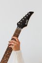 Crop anonymous female musician wearing white knitted sweater and wedding ring with modern electric guitar fretboard on white background