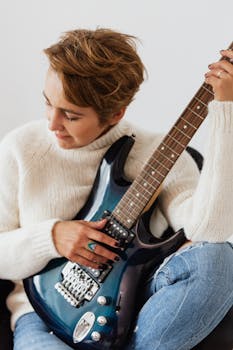 A woman in casual clothing playing an electric guitar in a cozy indoor setting.
