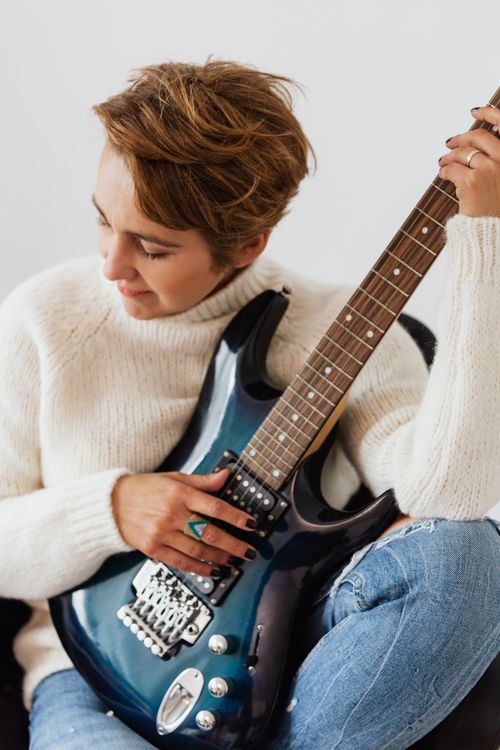 Free Content smiling female musician wearing casual jeans and white sweater playing guitar while sitting on white background Stock Photo