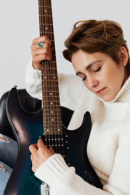 Free Content glad female guitarist in white knitted sweater with eyes closed sitting on chair with electric guitar against white background Stock Photo