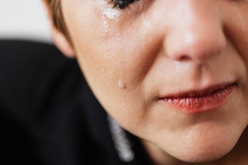 Closeup of crop anonymous sad adult female with makeup crying because of emotional problems