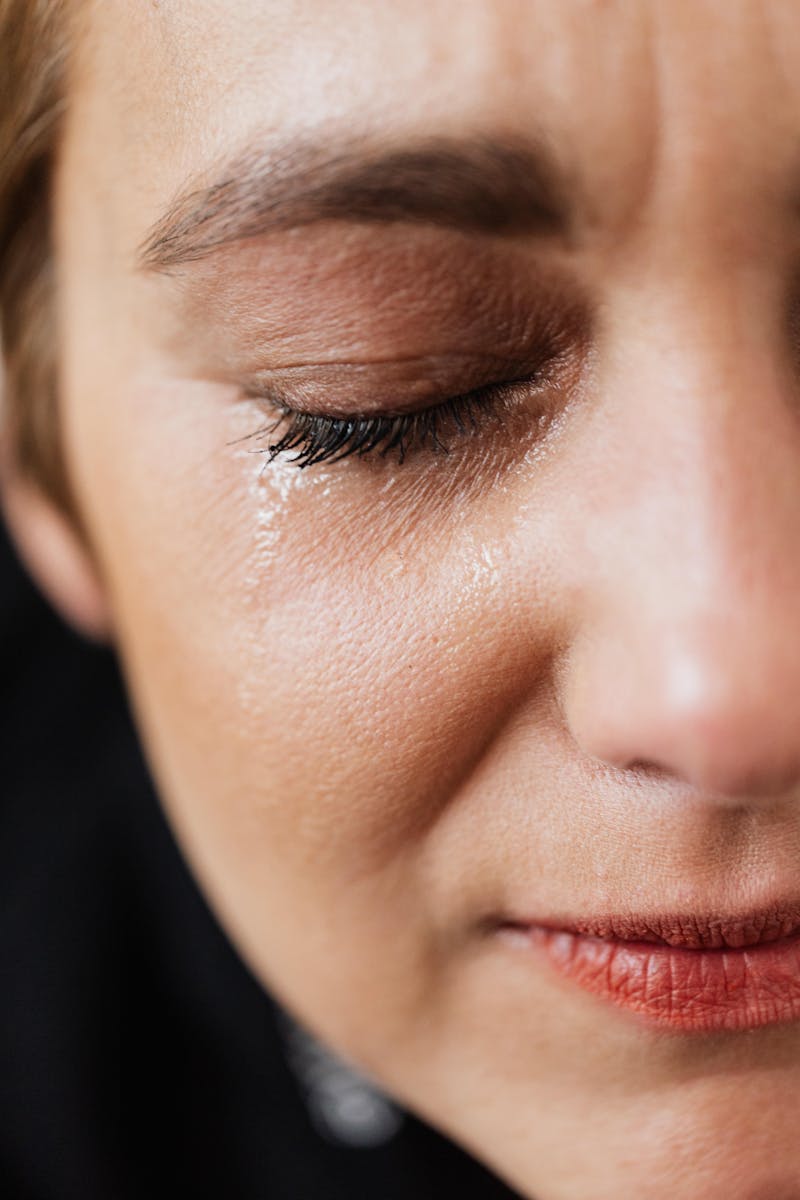 Closeup of crop sad adult lady with natural makeup having problems and crying alone