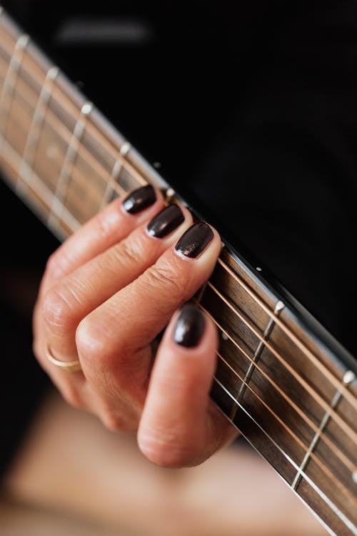 High angle of crop anonymous female musician with dark manicure performing song on electric guitar during music lesson