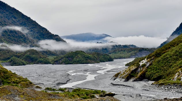Breathtaking landscape of Franz Josef Glacier with misty mountains and a flowing river in New Zealand.