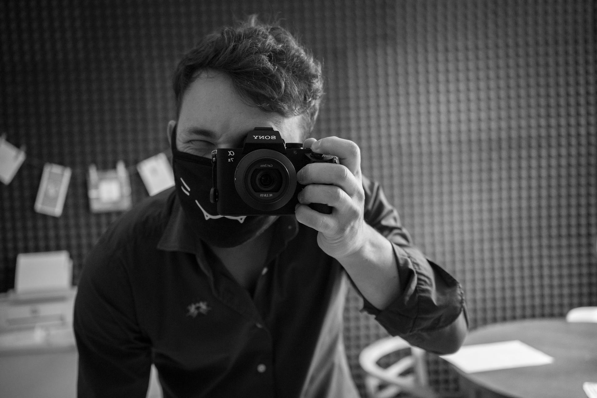 A man in a mask taking a photo indoors, highlighting technical photography elements.