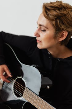 A thoughtful musician in a black hoodie plays an acoustic guitar.