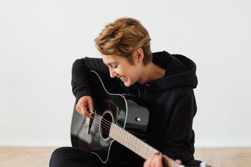 Free Smiling musician in a black hoodie plays an acoustic guitar with joy. Stock Photo