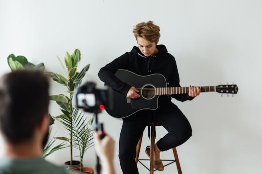 A musician sits on a wooden stool playing an acoustic guitar during a photo session.