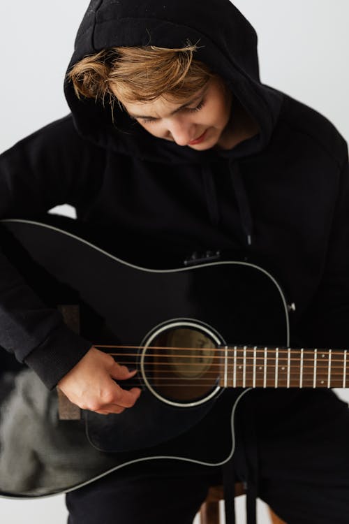Free Person in Black Hoodie Playing Acoustic Guitar Stock Photo