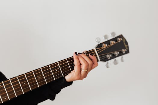 A close-up shot of a person playing an acoustic guitar, focusing on the hand and strings.